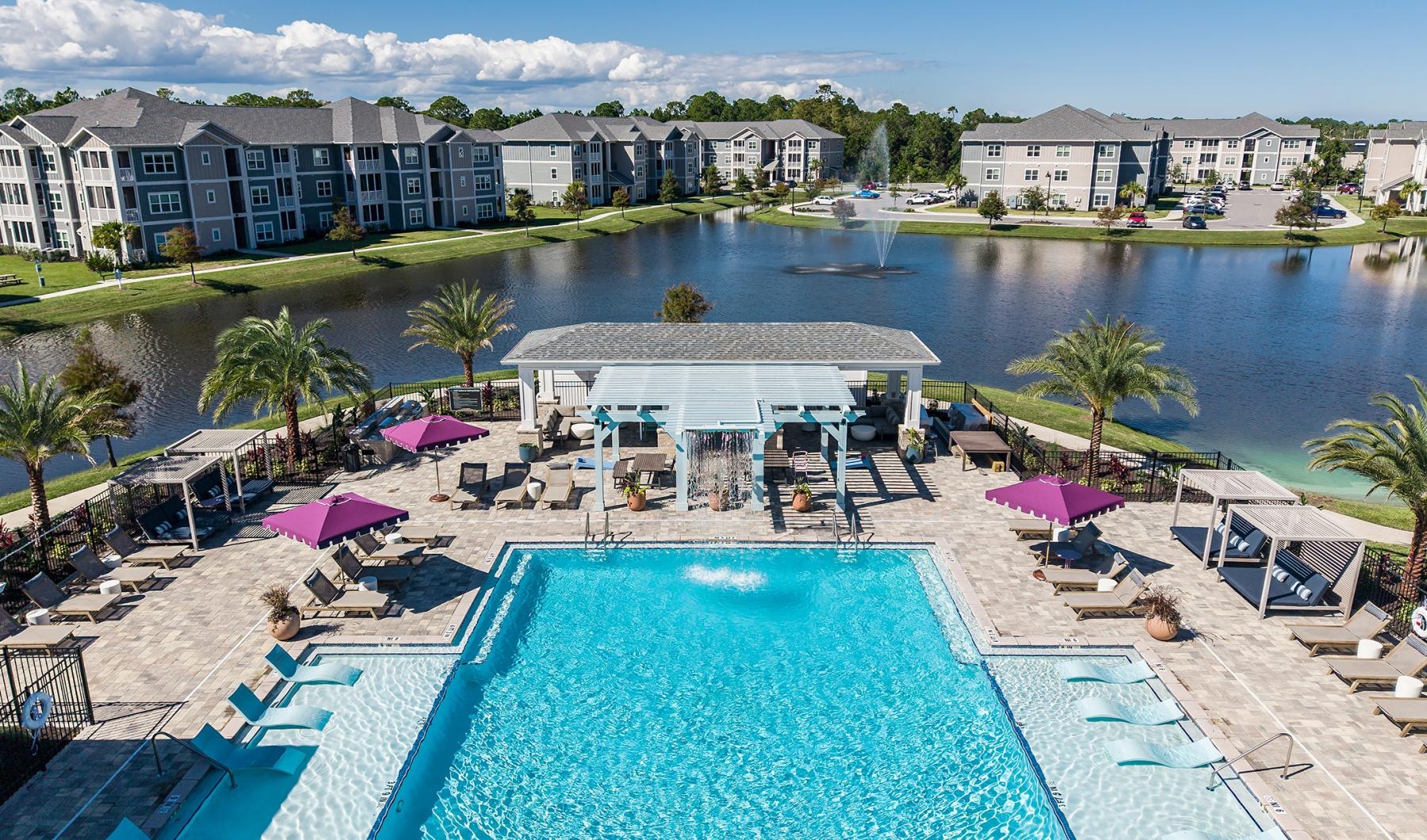 a pool with lounge chairs and umbrellas by a large building